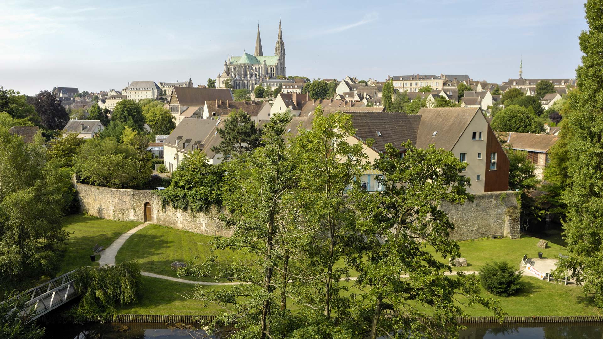 Vue sur la cathédrale depuis la rivière, avec un square arboré et l'ancien rempart de la ville